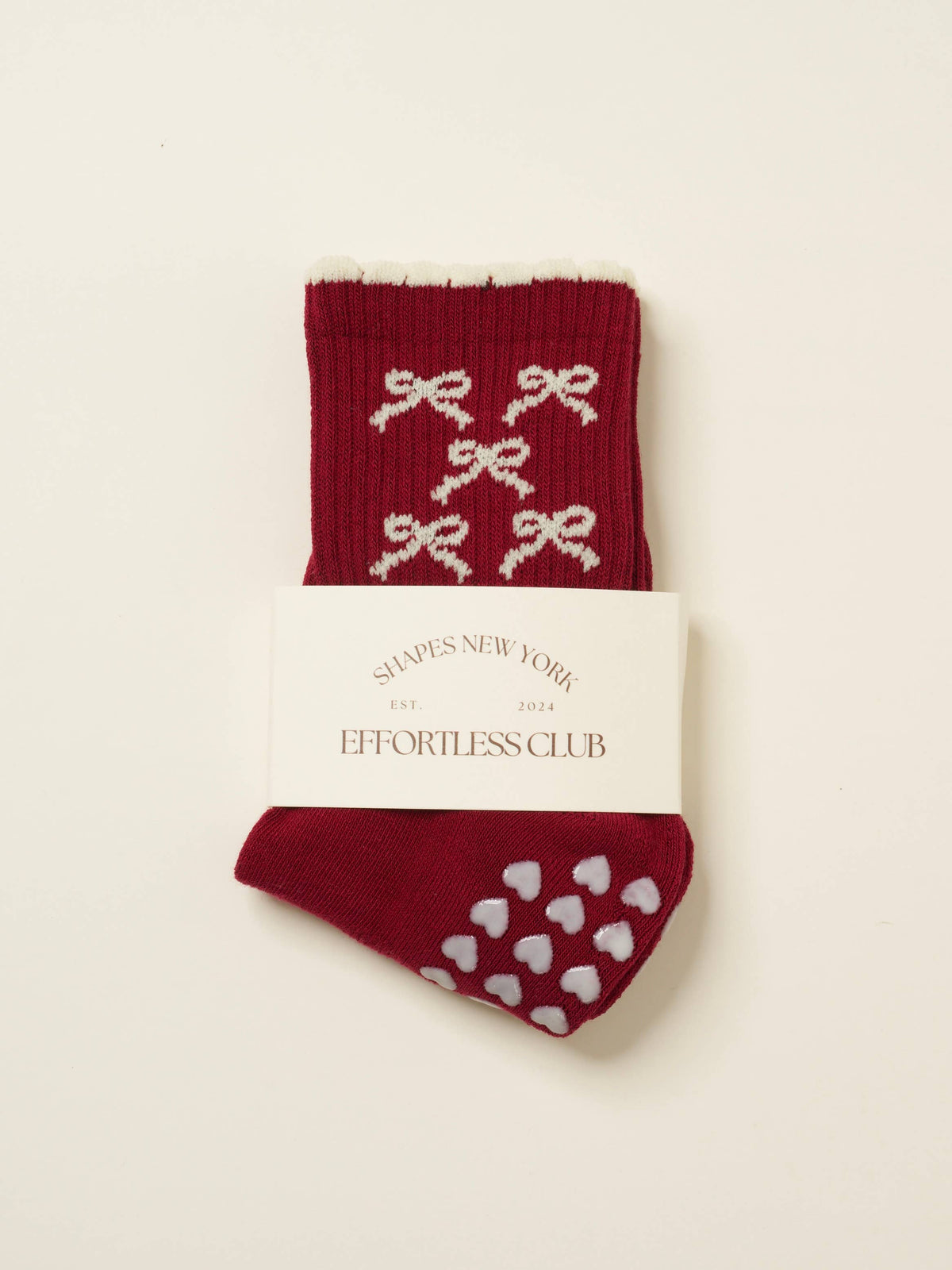 Burgundy knit grip socks with a pattern of small white bows and white heart grips on the sole