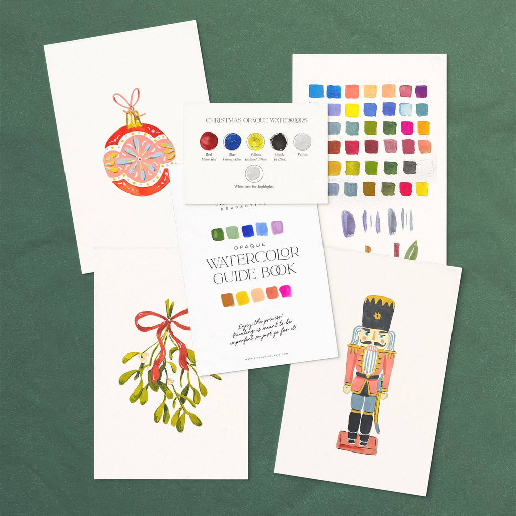 Christmas watercolor kit laid out: ornament, mistletoe and nutcracker designs with the guide book