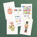 Christmas watercolor kit laid out: ornament, mistletoe and nutcracker designs with the guide book