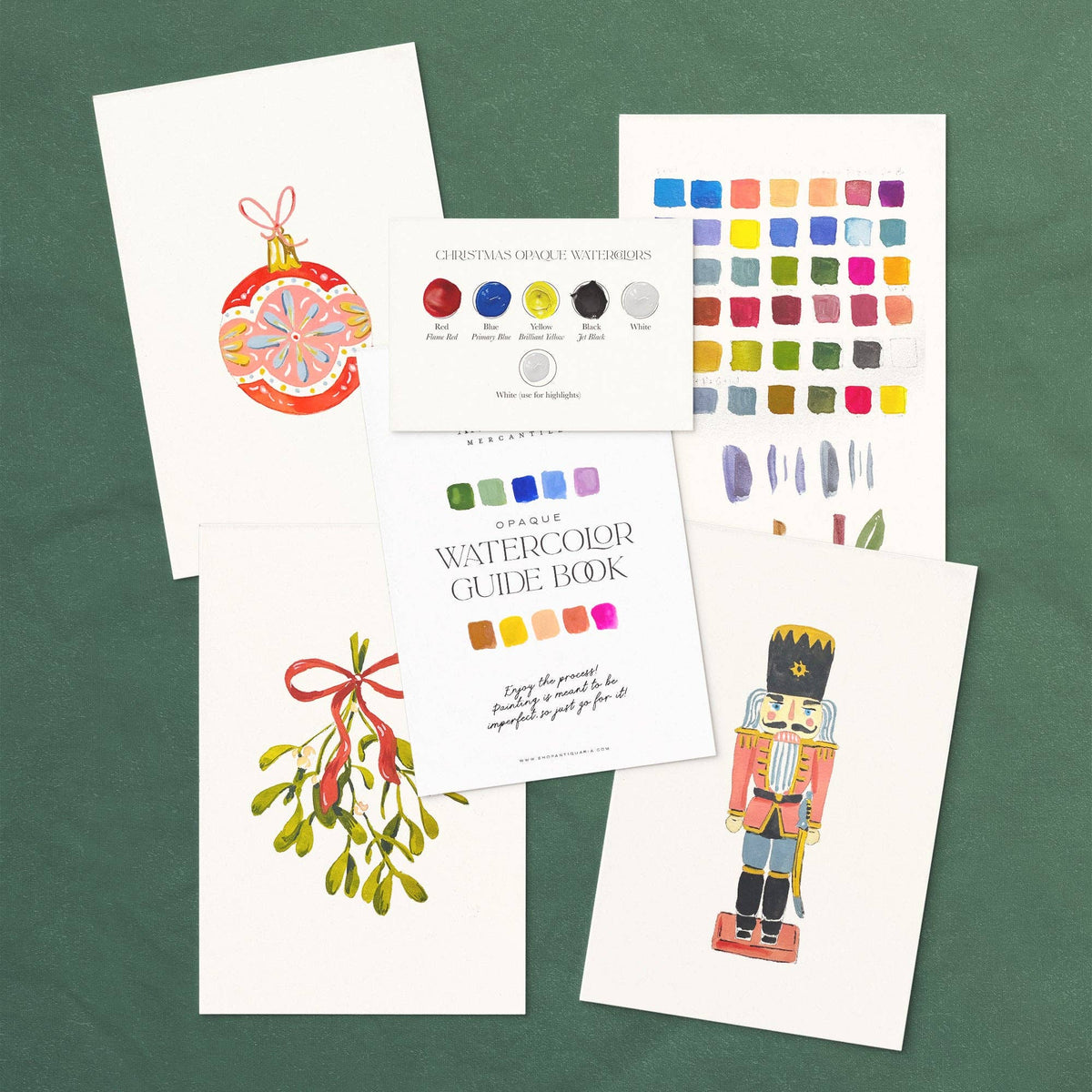 Christmas watercolor kit laid out: ornament, mistletoe and nutcracker designs with the guide book