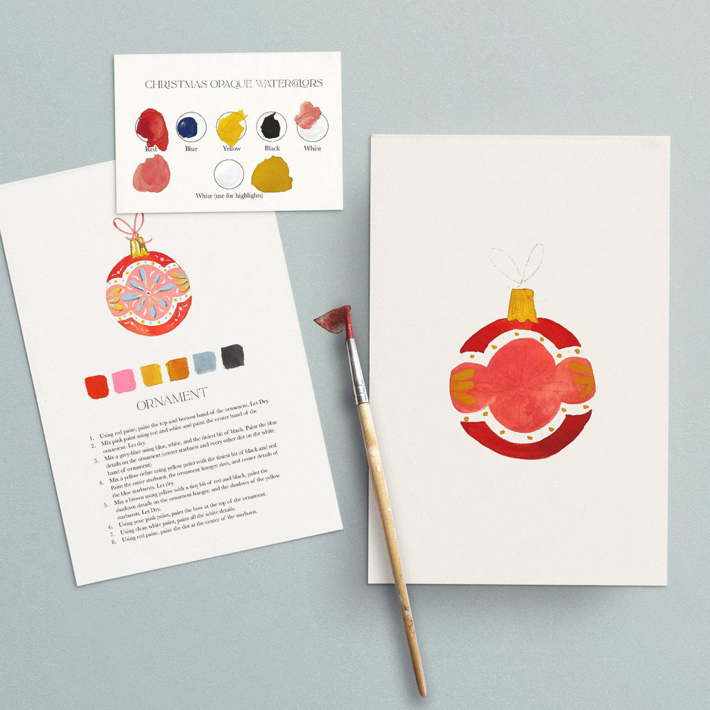 Instruction sheet for the ornament beside the finished red ornament painting and a brush