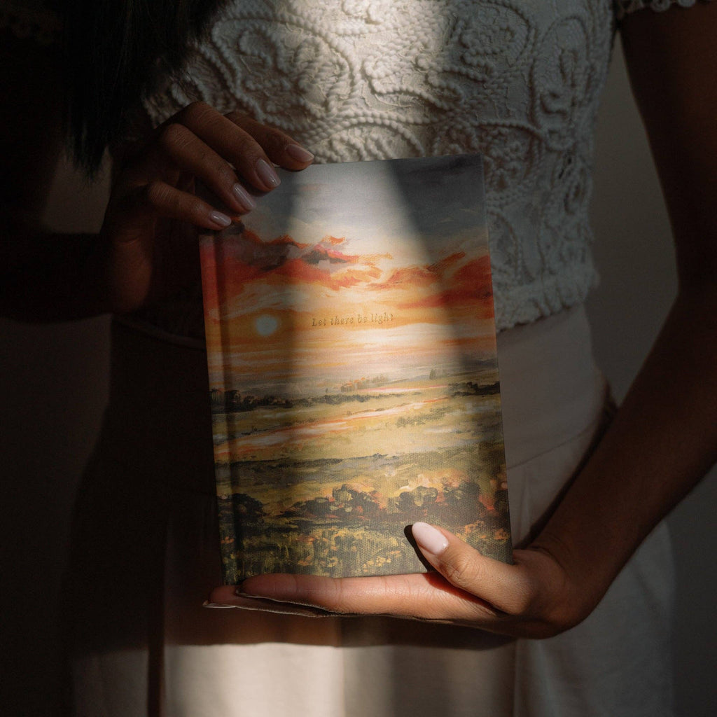 The sunset landscape notebook held against a white lace top