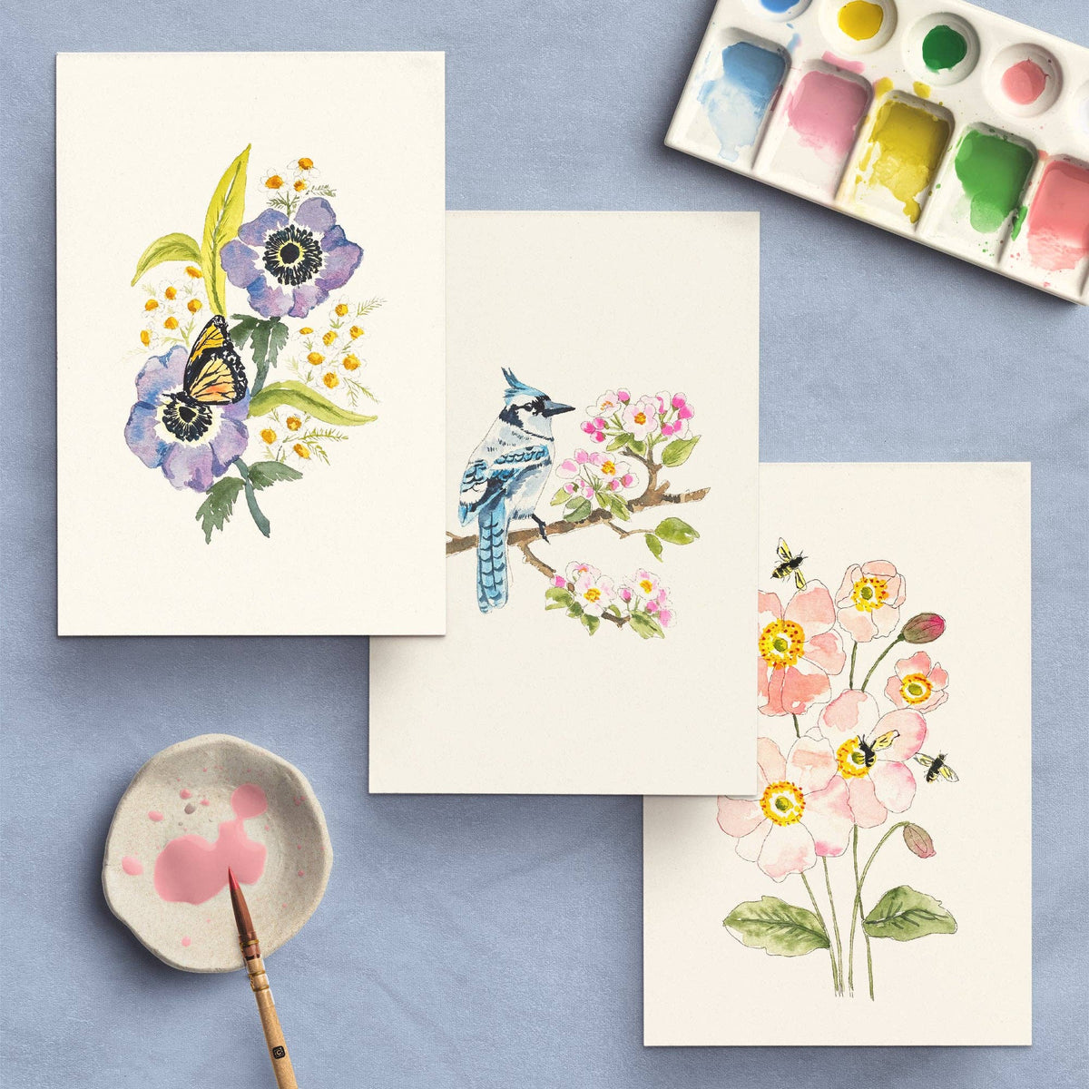 Three finished paintings: a butterfly on flowers, a blue jay on a branch and a bee among poppies