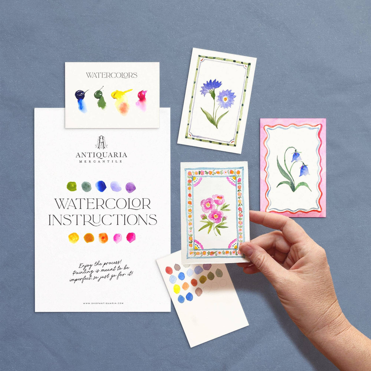 Hand holding the painted peony card beside the kit's instructions and other designs