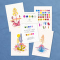 Cactus watercolor kit laid out: three desert plant designs, guide book and paint swatches