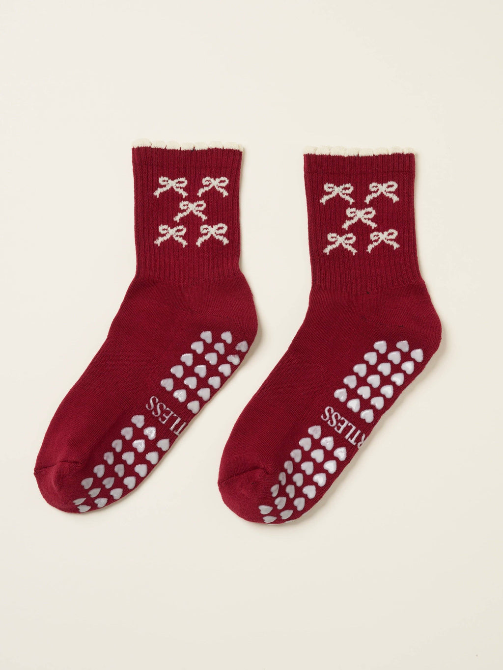 Pair of burgundy bow socks laid flat with cream heart grip soles