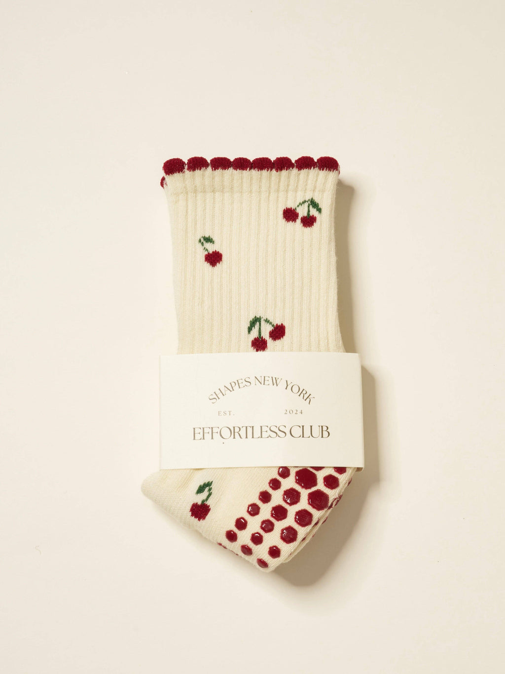Cream grip socks with red cherries and a red scalloped cuff, folded in their band