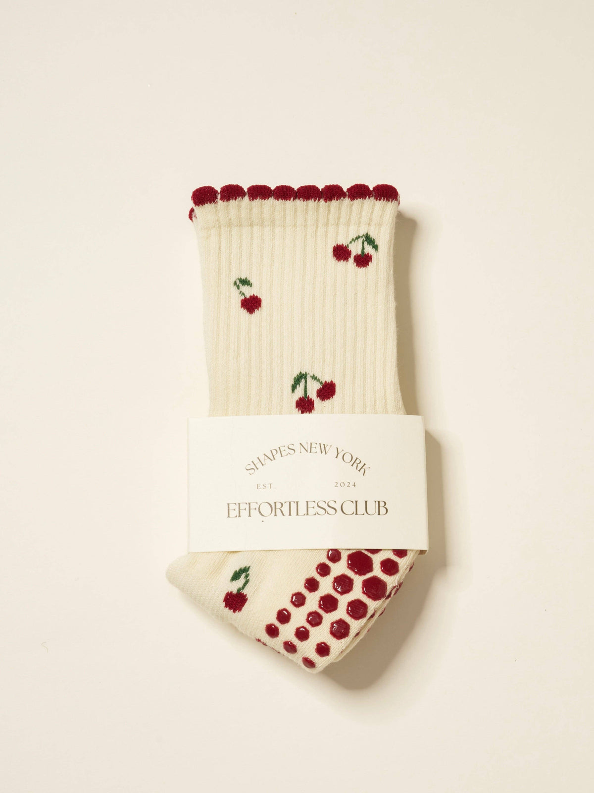 Cream grip socks with red cherries and a red scalloped cuff, folded in their band