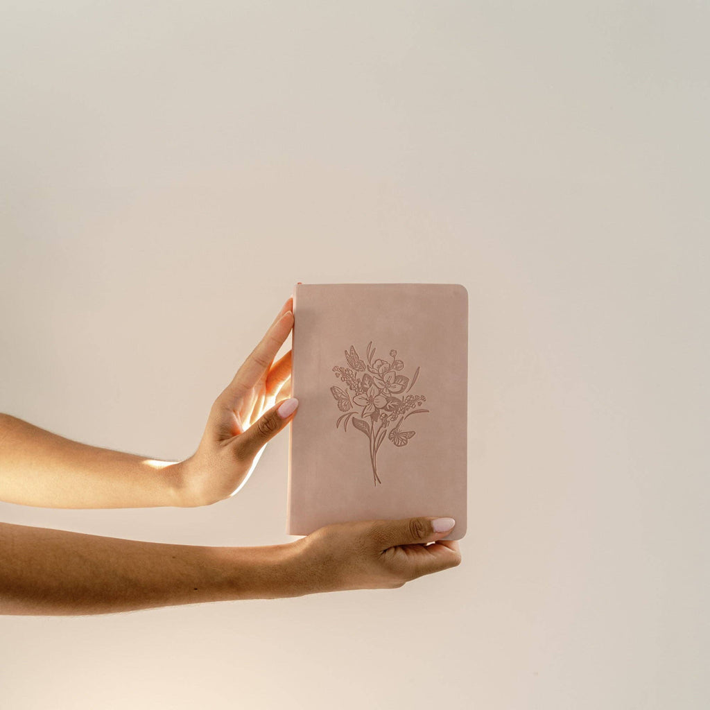 Hand holding the blush notebook against a cream wall
