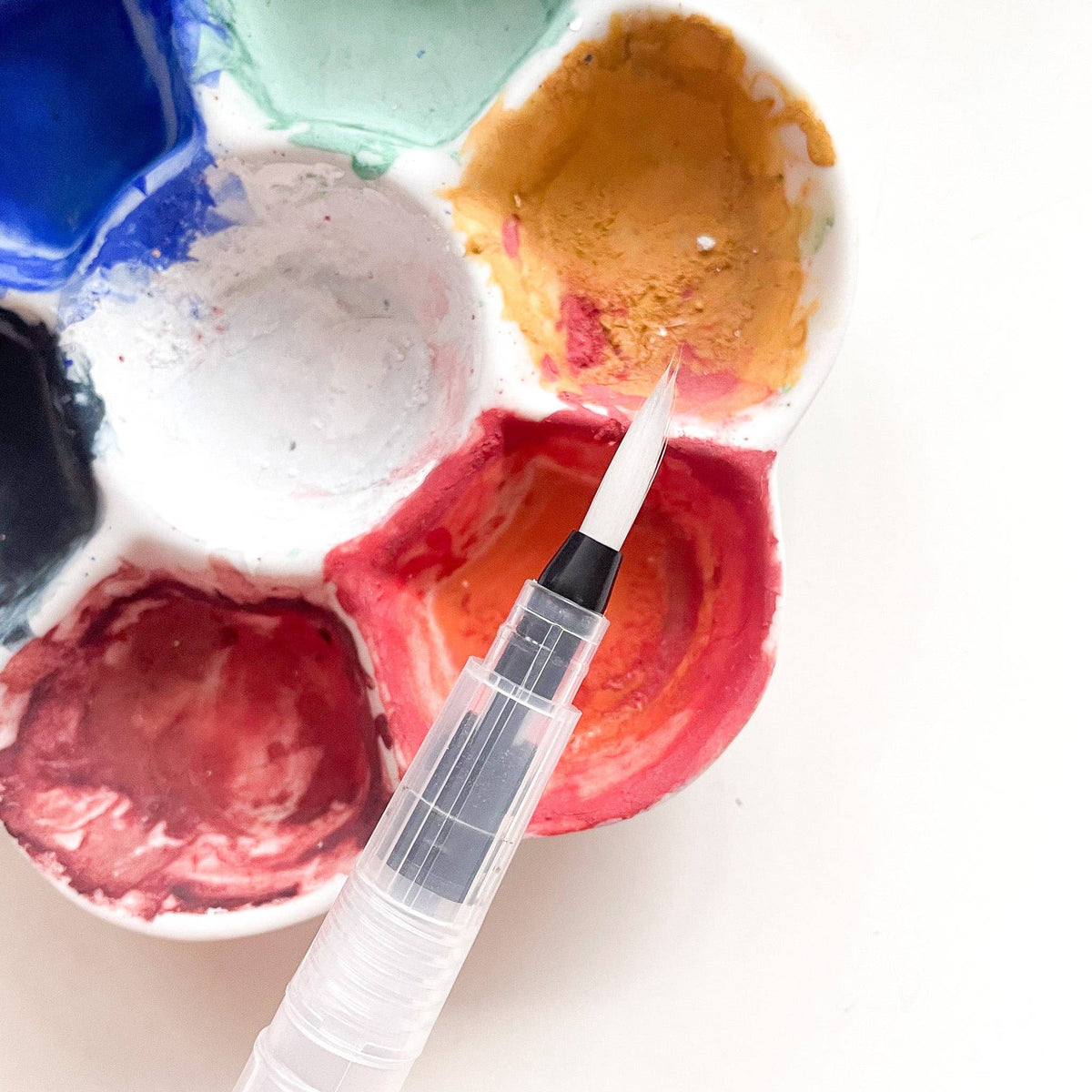 A water brush picking up red paint from a watercolor palette