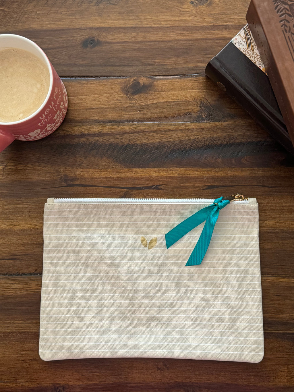 The cream striped zip pouch with a teal ribbon pull, closed