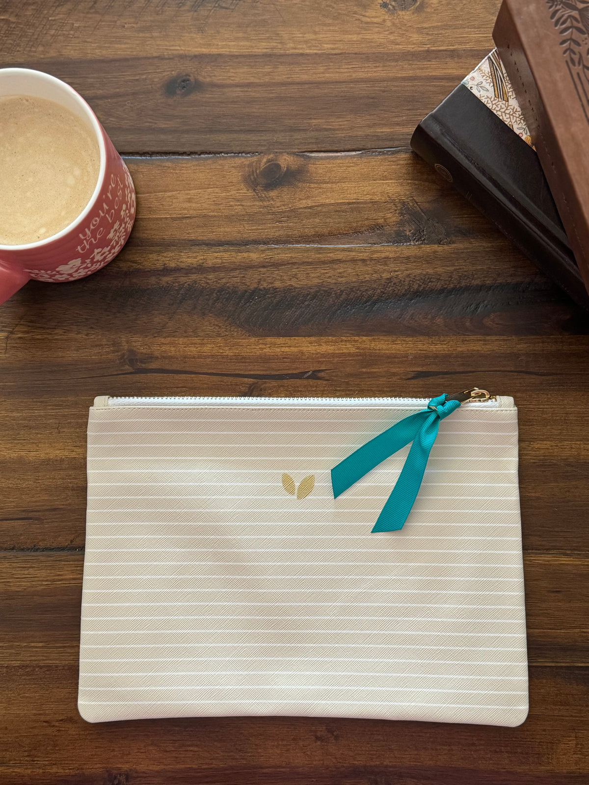 The cream striped zip pouch with a teal ribbon pull, closed