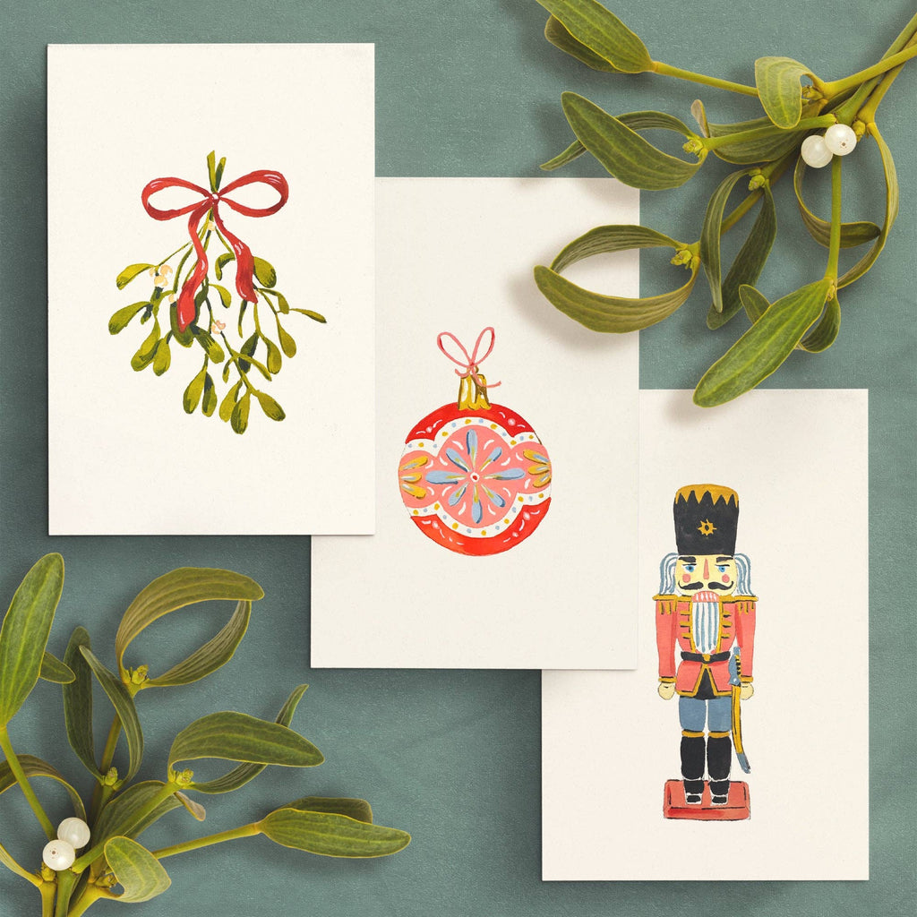 Three finished paintings: mistletoe tied with a red bow, a red ornament and a nutcracker