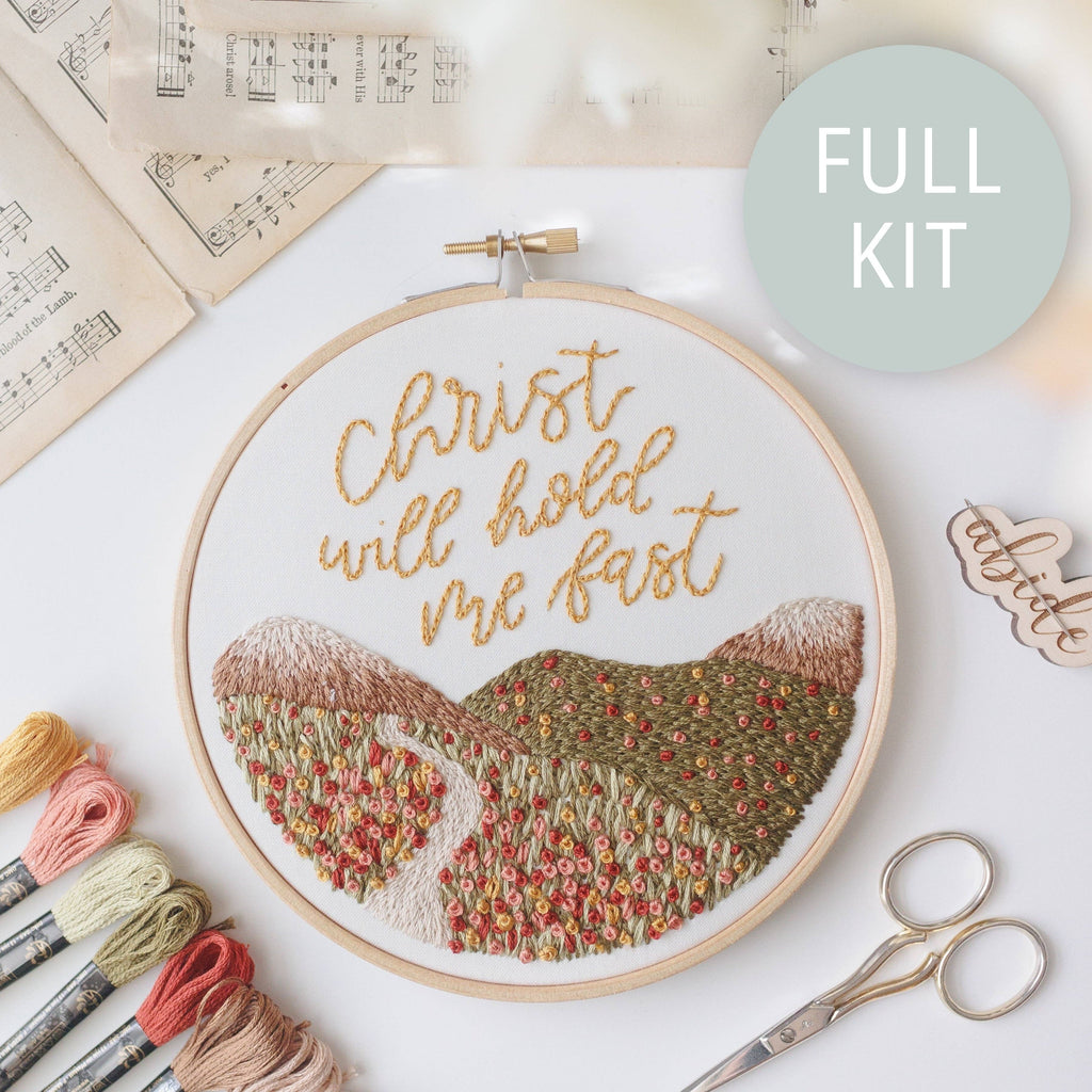 Finished hoop: "Christ will hold me fast" in gold script above stitched rolling hills and a path