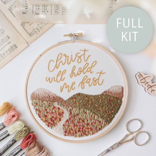Finished hoop: "Christ will hold me fast" in gold script above stitched rolling hills and a path