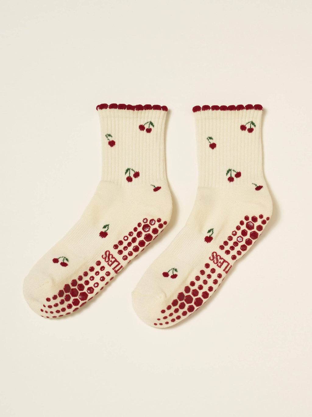 Pair of cream cherry socks laid flat with red grip soles