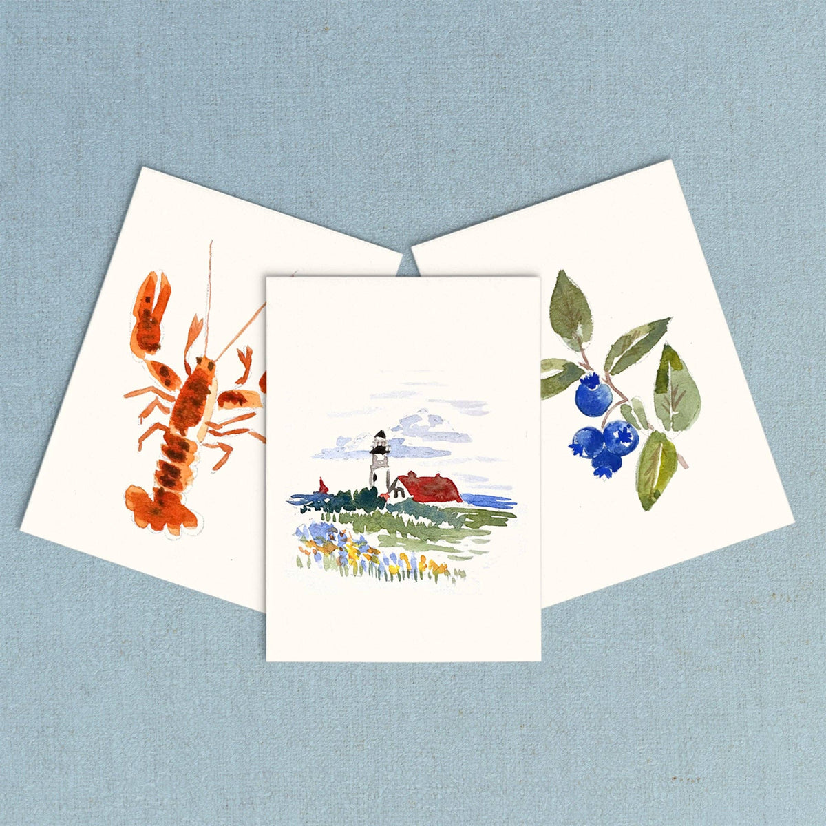 Three finished mini paintings: a red lobster, a coastal lighthouse and blueberries