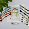 Snowman needlepoint kit: a painted canvas of a snowman in a brown hat and green scarf, with threads and tools
