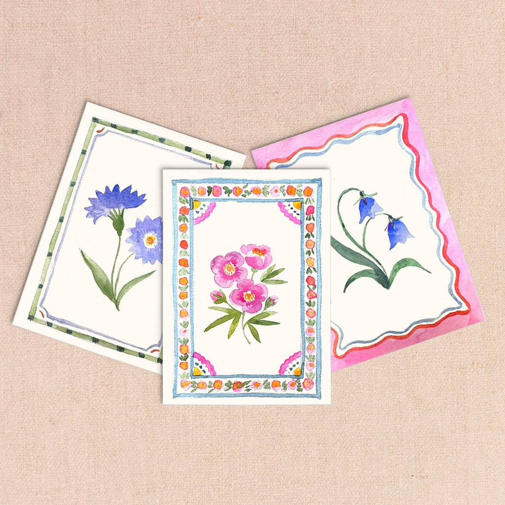 Three finished mini paintings: cornflowers, a pink peony with a floral border, and bluebells