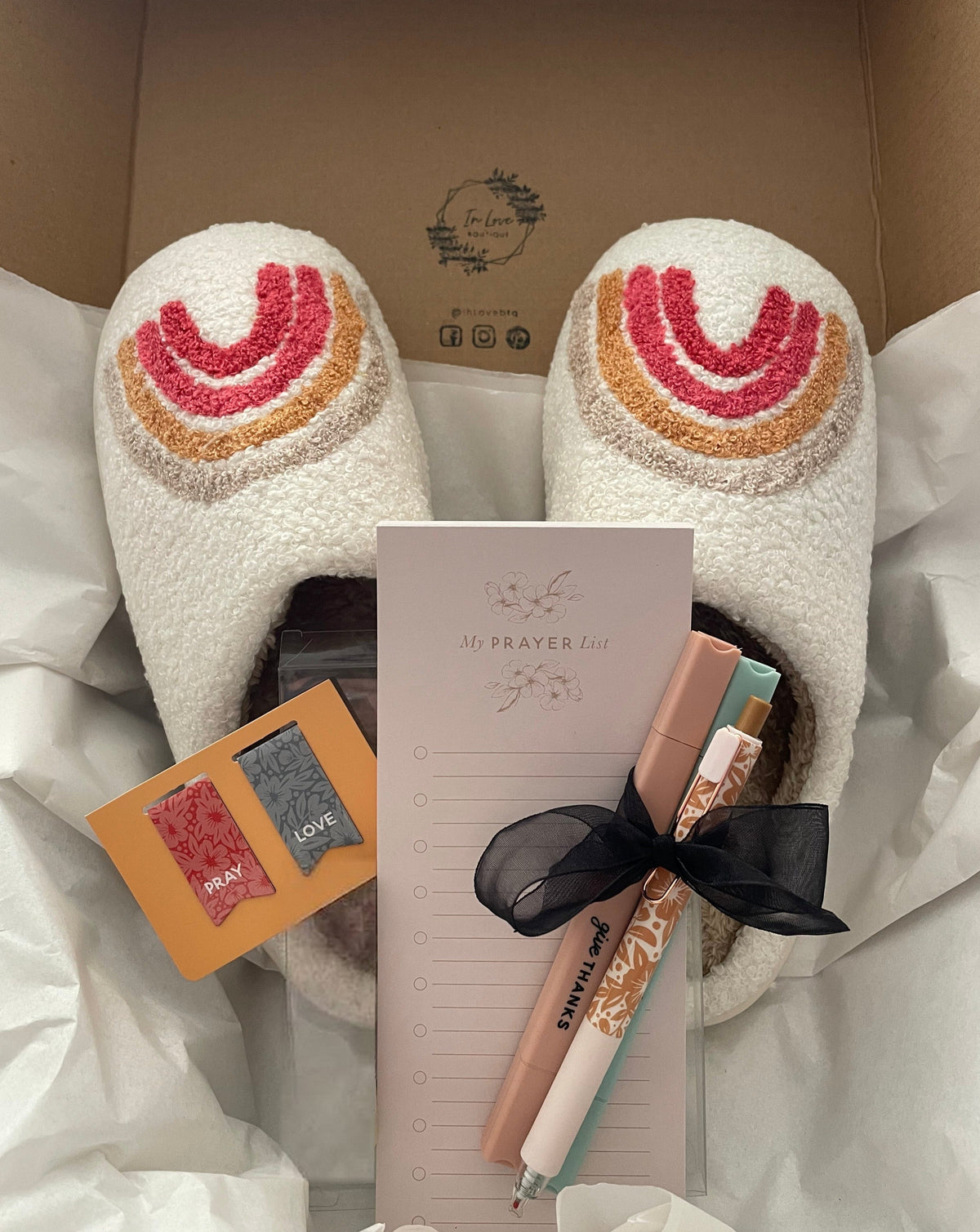 Study box contents packed in tissue: white slippers with a rainbow design, a My Prayer List pad, two pastel highlighters and a floral pen tied with a black ribbon, and Pray and Love magnetic bookmarks