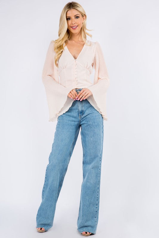 Blush V-neck top with covered buttons and pleated bell sleeves, worn with wide-leg jeans