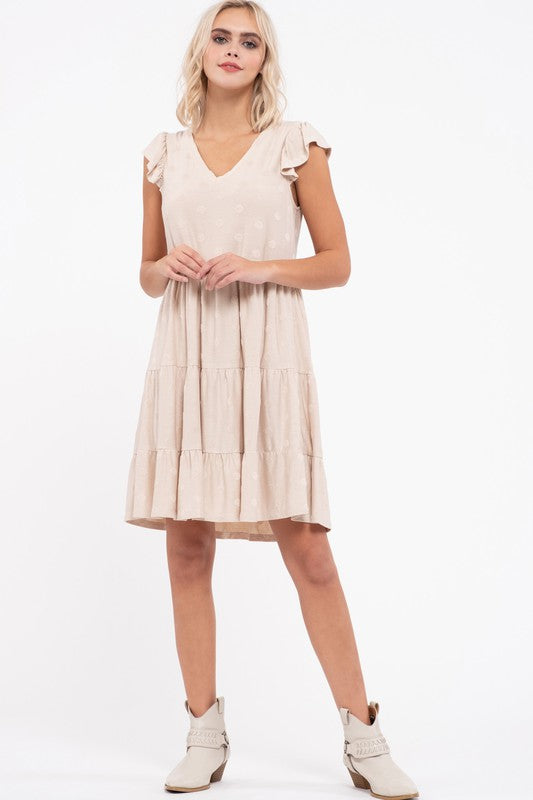 Cream tiered knee-length dress with a V-neck and flutter sleeves, worn with white boots