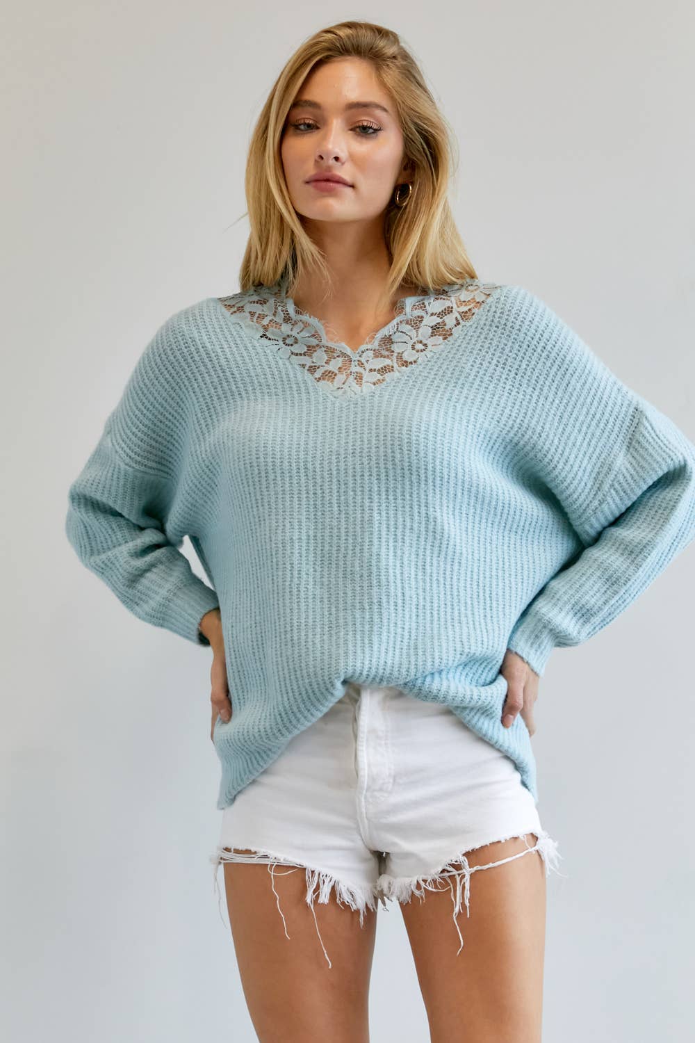 Pale blue V-neck knit sweater with lace trim at the neckline, worn with white shorts
