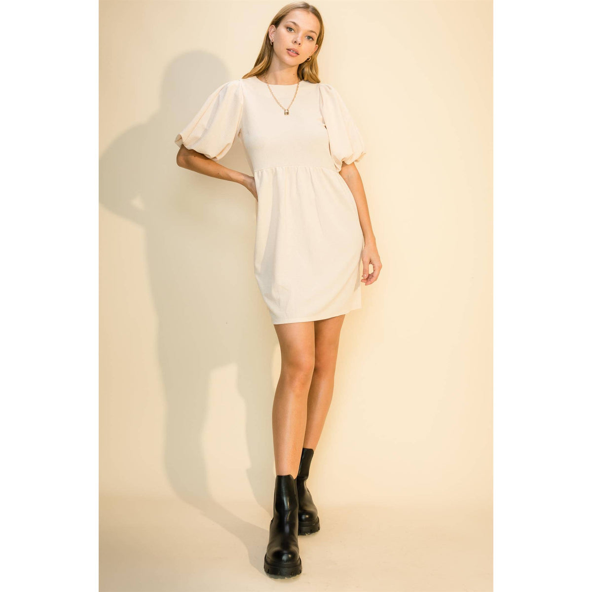 Cream babydoll mini dress with a round neck and puff sleeves, worn with black boots